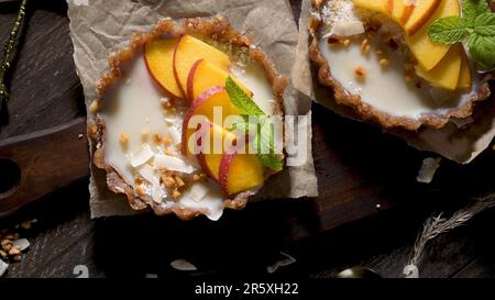 Vegane Pfirsichtörtchen mit geriebener Kokosnuss und knusprigen Erdnüssen. Obstkuchen. Dattel, Walnuss-, Mandel- und Haselnussbasis. Stockfoto