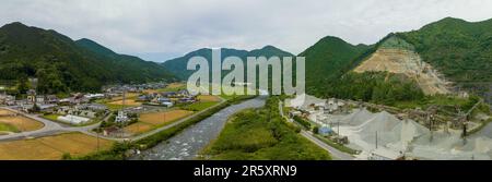 Materialhaufen im Tagebau am Fluss und Dorf in Berglandschaft Stockfoto