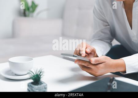 Social-Media-Tageskonzept. Weibliche Freiberuflerin, die den Tag früh beginnt, im Wohnzimmer für eine Website mit Smartphone. Geschäftsfrau, die im Home Offic arbeitet Stockfoto