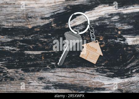 Hausschlüssel an einem hausförmigen Schlüsselanhänger, der auf Holzfußböden ruht, Konzept für Immobilienvermietung. Hausmodell und Schlüssel in Haustür. Echt Stockfoto