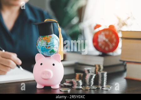 Graduierungskappe mit Kugel auf pinkfarbenem Sparschwein mit Münzstapel. Konzept der Kostenersparnis für ein Stipendium für ein Studium im Ausland. Finanziell Stockfoto