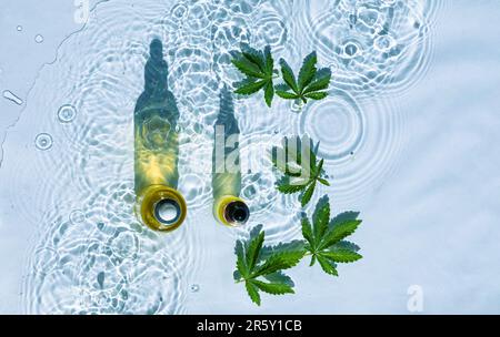 CBD-Ölflaschen, blauer Wasserhintergrund mit Tropfen, Wellen und Blättern aus Hanf, Marihuana Stockfoto