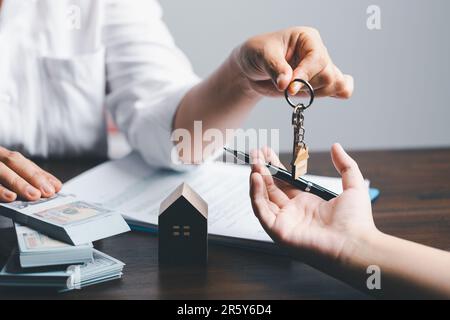 Der Hausmakler hält die Schlüssel und das Modellhaus wird den Kunden ausgehändigt. Hausmodell mit Immobilienmakler mit Kunde für s. Stockfoto