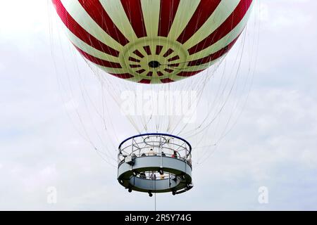 Schwebende rot-weiße Ballon-Nahaufnahme. Hängekorb und Aussichtsplattform mit Menschen. Aufhängungsseile. Besichtigungstour in Budapest Stockfoto