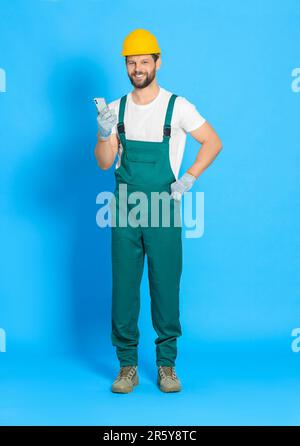 Professioneller Mechaniker in Uniform mit Smartphone auf hellblauem Hintergrund Stockfoto