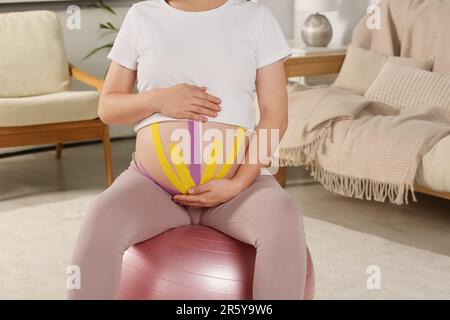 Schwangere Frau mit Kinesio-Videos, die zu Hause Sportball-Übungen macht, Nahaufnahme Stockfoto