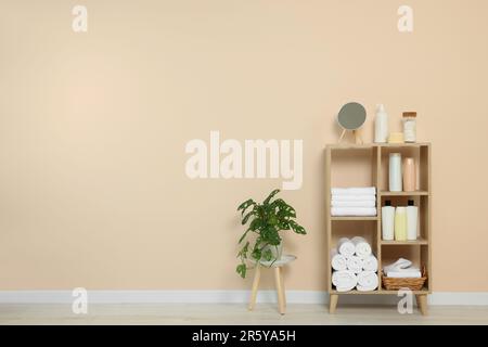Weiche gefaltete Handtücher und Kosmetikflaschen auf Holzregalen nahe beigefarbener Wand, Platz für Text Stockfoto