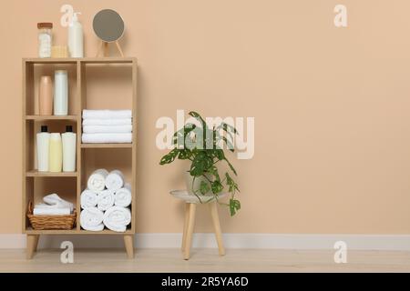 Weiche gefaltete Handtücher und Kosmetikflaschen auf Holzregalen nahe beigefarbener Wand, Platz für Text Stockfoto