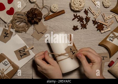 Eine nicht erkennbare junge Frau malt Zahlen auf Kerzen. Frau macht hausgemachte Adventskalender mit eigenen Händen gemacht Schritt für Schritt selbstgemachtes Kunsthandwerk Machen Sie es selbst. Vorbereitung auf das weihnachtskonzept. Saisonale Aktivitäten für Kinder, Familienurlaub im Winter. Umweltfreundlich Geschenke. Öffnen Sie das Paket jeden Tag Stockfoto