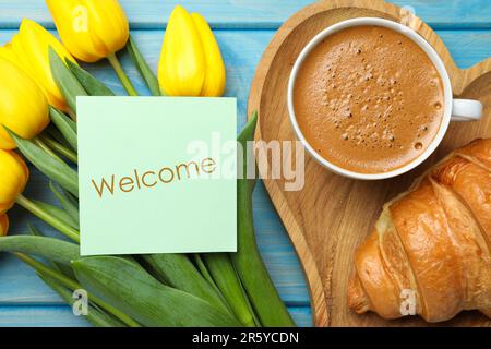 Begrüßungskarte, wunderschöne gelbe Tulpen, Croissant und eine Tasse aromatischen Kaffee auf einem hellblauen Holztisch, flach liegend Stockfoto