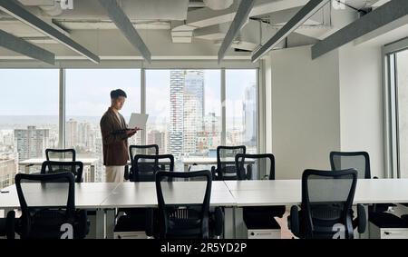 Junger, seriöser asiatischer Geschäftsmann, der im Büro an einem Laptop arbeitet. Stockfoto