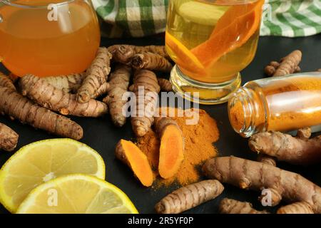 Kurkumwurzeln, Pulver, Zitronenscheiben und eine Tasse leckeren Tees auf dem schwarzen Tisch Stockfoto