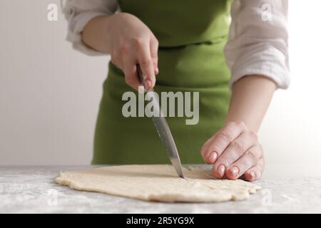 Frau schneidet Teig auf einem hellgrauen Marmortisch, Nahaufnahme. Ich koche Grissini Stockfoto