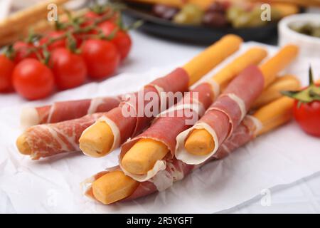 Köstliche Grissini-Sticks mit Prosciutto und Snacks auf weißem Tisch, Nahaufnahme Stockfoto