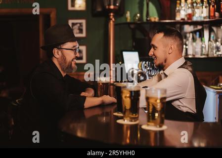 Der Mann hat Spaß, sich mit einem Barkeeper an der Bar bei einem Glas Bier in einem Pub zu unterhalten Stockfoto