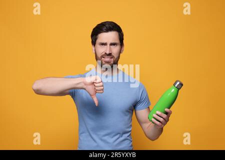 Mann mit grüner Wärmflasche, Daumen nach unten auf orangefarbenem Hintergrund Stockfoto