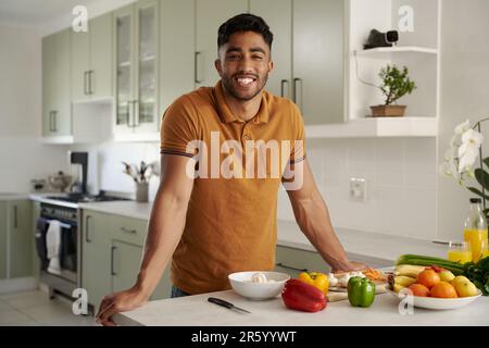 Glücklicher junger birassistischer Mann in lässiger Kleidung, der neben Essen in der Küche auf die Kamera schaut Stockfoto
