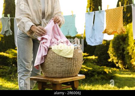 Eine Frau hängt Babykleidung mit Wäscheklammern an der Wäscheleine auf, um im Garten zu trocknen, zu schließen Stockfoto