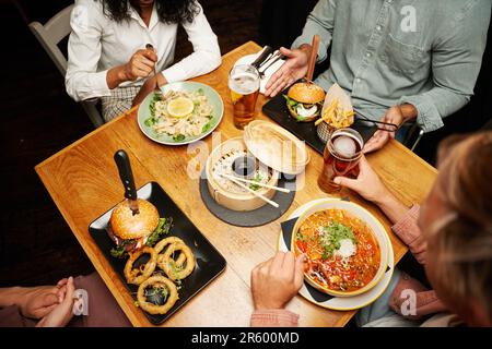 Junge, multiethnische Gruppe von Freunden in legerer Kleidung, die mit Bier und Abendessen im Restaurant sitzen Stockfoto