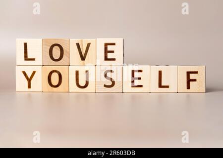 Das Wort LIEBE DICH SELBST auf Holzwürfeln auf einem beigefarbenen neutralen Studiohintergrund. Bereich Kopieren. Geschrieben. Textwörter sind wichtig. Psychische Gesundheit des Menschen. Hautpflege Bod Stockfoto