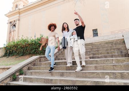 Eine Gruppe aus verschiedenen multiethnischen Schülern, die unten auf dem Campus zusammen spazieren, reden, zeigen und lächeln. Junge asiatische Teenagerin mit zwei männlichen Freunden, die sich nach dem Unterricht unterhalten. Hochwertiges Foto Stockfoto
