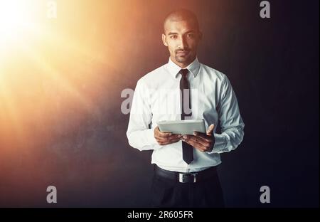 Moderne Unternehmen müssen immer in Verbindung bleiben. Studioporträt eines jungen Geschäftsmannes mit einem digitalen Tablet vor dunklem Hintergrund. Stockfoto