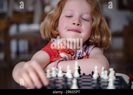 Ein rothaariges Mädchen, das Schach spielt und über den nächsten Schritt nachdenkt. Differenzfokus, Nahaufnahme. Stockfoto