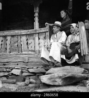 Maramures County, Sozialistische Republik Rumänien, ca. 1980. Ältere Paare und ihre Tochter auf der Veranda ihres traditionellen Holzhauses. Stockfoto
