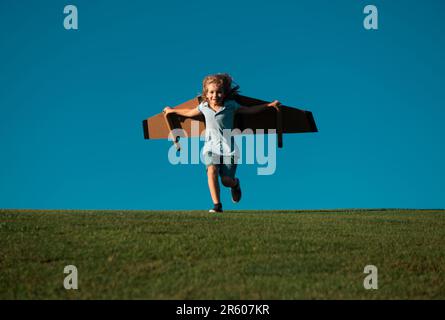 Kinderreisender mit Rucksackflügeln. Kind spielt Flieger und träumt im Park. Kleiner Junge Pilot gegen einen blauen Himmel. Stockfoto