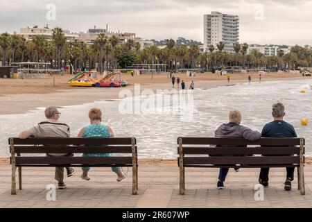 Zwei Paare, die vier auf Bänken an der Promenade des Yachthafens sitzen und den Levante-Strand des Mittelmeers in Salou, Tarragona, Spanien, betrachten. Stockfoto