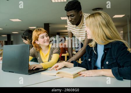 Verschiedene Schüler sitzen in der Bibliothek mit einem Laptop Stockfoto