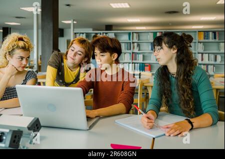 Verschiedene Schüler arbeiten an einem Laptop für ein Projekt in der Bibliothek Stockfoto