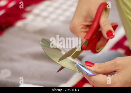 Frau schneidet alte CDs mit einer Schere zu Hause aus nächster Nähe Stockfoto