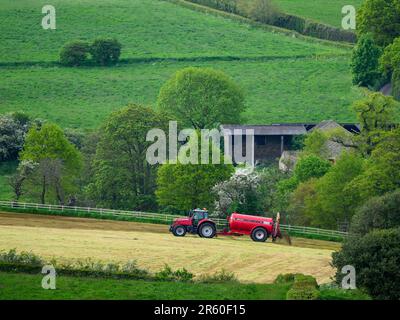 Landwirt arbeiten Fahren Traktor & zylindrischen Düngebehälter Sprühen Entleerungs Gülle auf Land Ackerland Weide Gras - Yorkshire, England Großbritannien Stockfoto