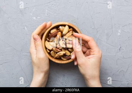 Frauenhände, die eine Holzschüssel mit brasilien- oder bertholletia-Nüssen halten. Gesundes Essen und Snack. Vegetarische Snacks mit verschiedenen Nüssen. Stockfoto