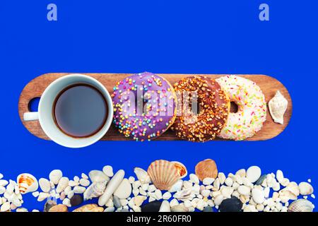 Verschiedene Donuts und eine Tasse Kaffee auf einer Tafel auf blauem Hintergrund. Seegrenze. Stockfoto