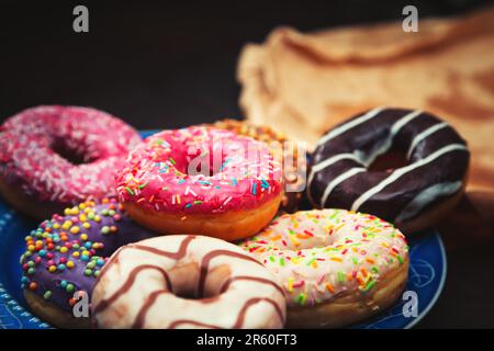 Teller mit verschiedenen Donuts auf dem Holztisch. Lebensmittelhintergrund. Stockfoto