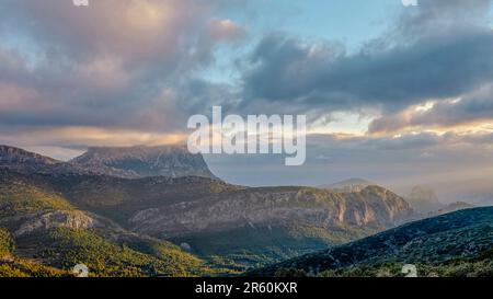 Berge und ein wunderschöner Himmel mit Sonnenstrahlen über dem Berg Puig Campana. Mount Castellet auf der rechten Seite. In der Valencianischen Gemeinde, Alicante, Spa Stockfoto