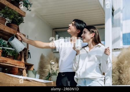 Liebhaber verbringen ihre Zeit damit, auf den stilvollen Balkonen auf dem Dach kleine Gärten, Pflanzen und frische Blumen zu bewässern. Entspannen Sie sich in ordentlichem Raum. Mit der Natur zurechtkommen Stockfoto