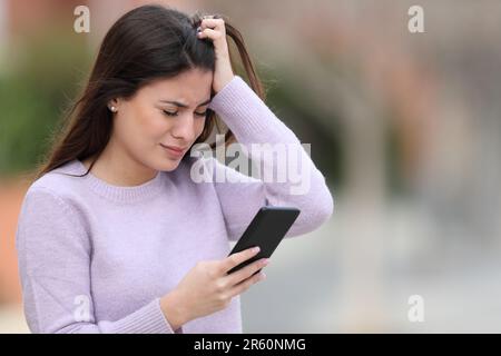 Trauriger Teenager, der sich beschwert, als er auf der Straße auf dem Smartphone stand Stockfoto