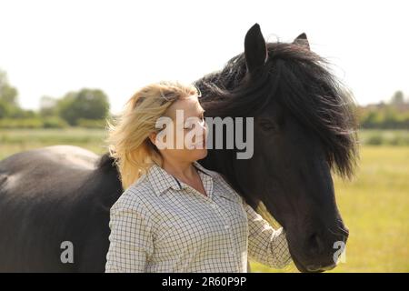 Eine blonde Frau, die ein schwarzes Pony umarmt Stockfoto