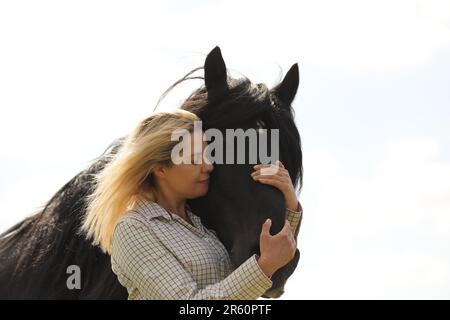 Eine blonde Frau, die ein schwarzes Pony umarmt Stockfoto