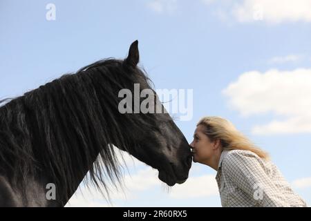 Eine blonde Frau, die ein schwarzes Pony umarmt Stockfoto