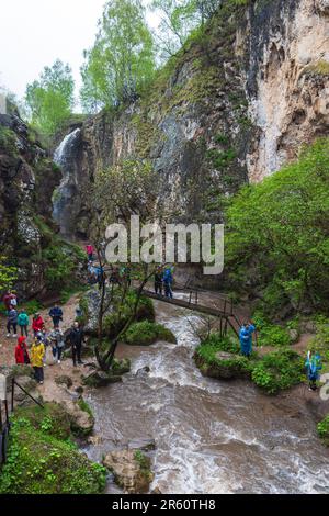 Karachay-Tscherkesien, Russland - 8. Mai 2023: Touristen gehen über die Brücke über den Bach. Honigwasserfälle sind eine Gruppe von Wasserfällen auf der Alikonovka und Stockfoto