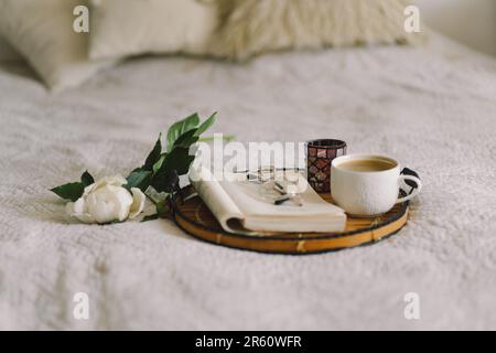 Offenes Buch mit Gläsern, Tasse Kaffee und Blumenstrauß mit weißen pinkfarbenen Pfingstrosen Stockfoto