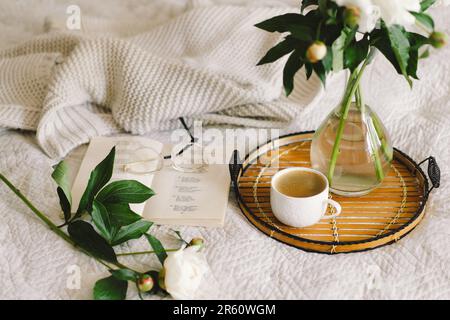 Offenes Buch mit Gläsern, Tasse Kaffee und Blumenstrauß mit weißen pinkfarbenen Pfingstrosen Stockfoto