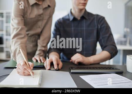 Nahaufnahme einer jungen Frau, die sich Notizen in Notizbuch macht, während sie ein Projekt im Büro, im Kopierbereich überprüft Stockfoto