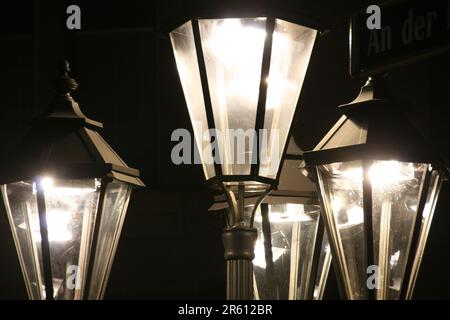 Drei Straßenlichter im traditionellen Stil beleuchten nachts ein Straßenschild vor einem dunklen Hintergrund Stockfoto