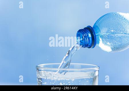 Aus dem Flaschenhals fließt frisches und kühles Wasser. Wasser wird aus einer Plastikflasche in ein Glas gegossen. Speicherplatz kopieren. Nahaufnahme Stockfoto