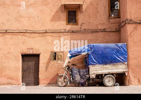 Ein gut gebrauchtes Motordreirad mit festem Anhänger und Markise, das vor einer Gasse in der Medina von Marrakesch, Marokko, geparkt ist. Stockfoto